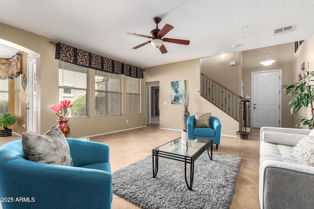 living area featuring visible vents, arched walkways, baseboards, ceiling fan, and stairs