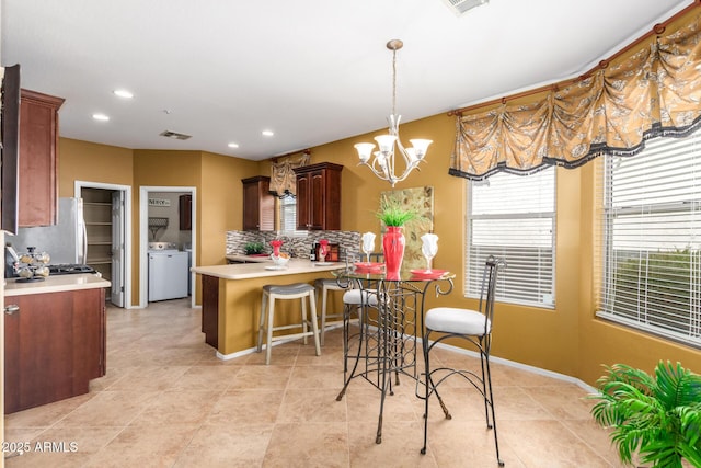 kitchen featuring freestanding refrigerator, light countertops, backsplash, and a peninsula