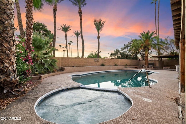 pool at dusk featuring a patio, a fenced backyard, and a pool with connected hot tub