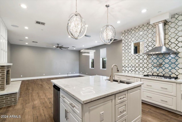 kitchen featuring visible vents, ceiling fan with notable chandelier, gas stovetop, wall chimney exhaust hood, and a sink