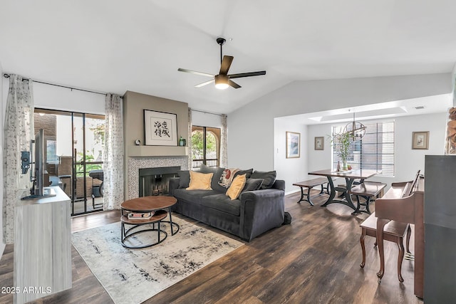 living room with lofted ceiling, dark wood-style floors, ceiling fan with notable chandelier, and a tile fireplace