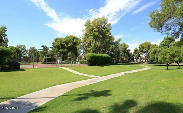 view of home's community with a tennis court, a yard, and fence