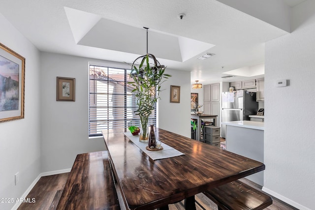 dining room with a tray ceiling, visible vents, baseboards, and wood finished floors