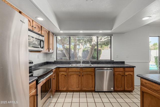 kitchen with stainless steel appliances, dark countertops, brown cabinetry, and plenty of natural light