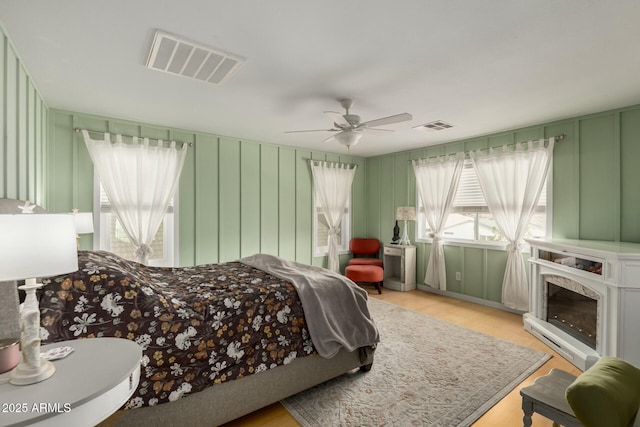 bedroom featuring a decorative wall, visible vents, light wood finished floors, and ceiling fan