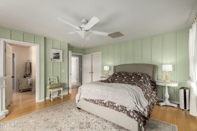 bedroom with a decorative wall, wood finished floors, visible vents, and ceiling fan