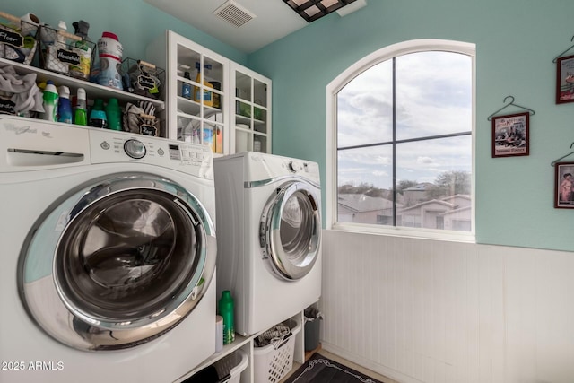 clothes washing area featuring wainscoting, laundry area, independent washer and dryer, and visible vents