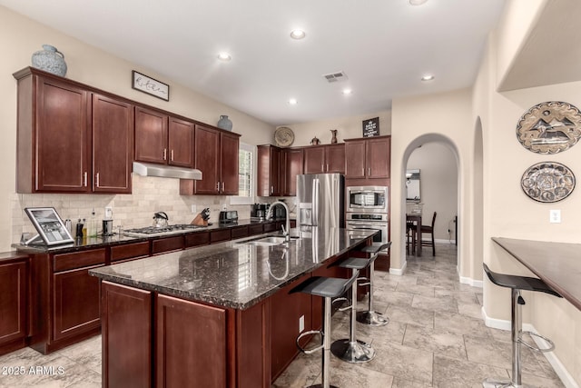 20532 W Summit Pl, Buckeye, AZ 85396 - kitchen with appliances with stainless steel finishes, a sink, a breakfast bar area, arched walkways, and dark stone counters