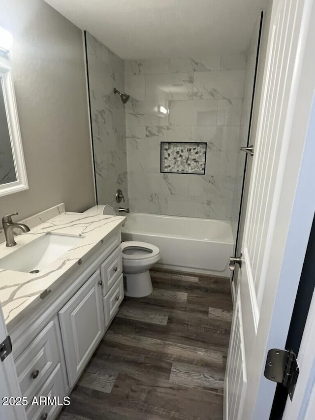 full bathroom with hardwood / wood-style flooring, tiled shower / bath, vanity, and toilet