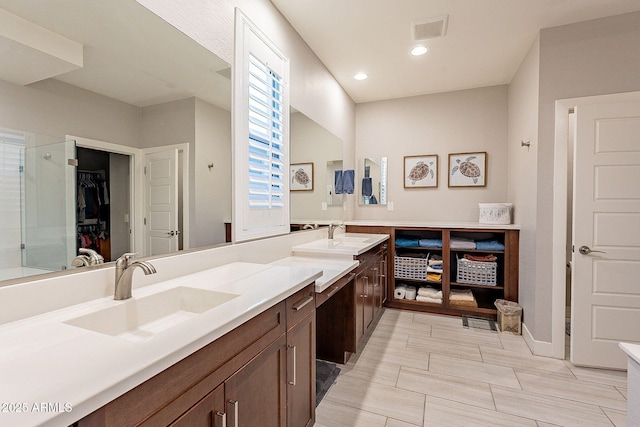 bathroom with double vanity, visible vents, a walk in closet, and a sink