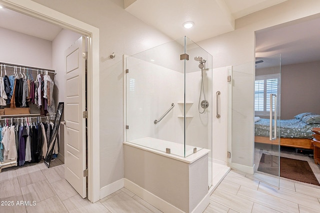 ensuite bathroom featuring ensuite bath, a stall shower, a walk in closet, and baseboards