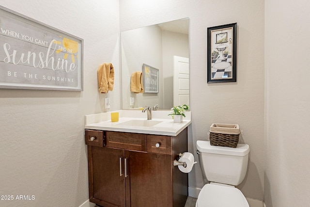 half bath featuring toilet, a textured wall, and vanity