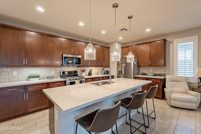 kitchen with a sink, visible vents, a kitchen breakfast bar, appliances with stainless steel finishes, and pendant lighting