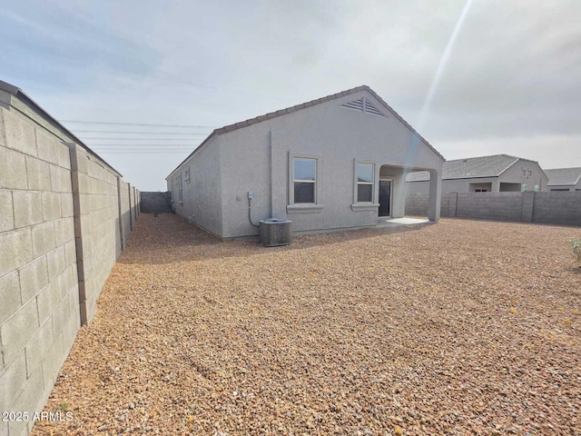 rear view of property featuring a fenced backyard, central AC, and stucco siding