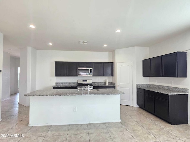 kitchen with a kitchen island with sink, light stone counters, appliances with stainless steel finishes, and visible vents