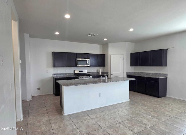 kitchen with stone countertops, recessed lighting, stainless steel appliances, visible vents, and an island with sink