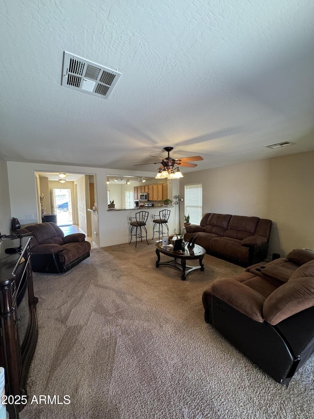 carpeted living room with a textured ceiling, ceiling fan, and visible vents