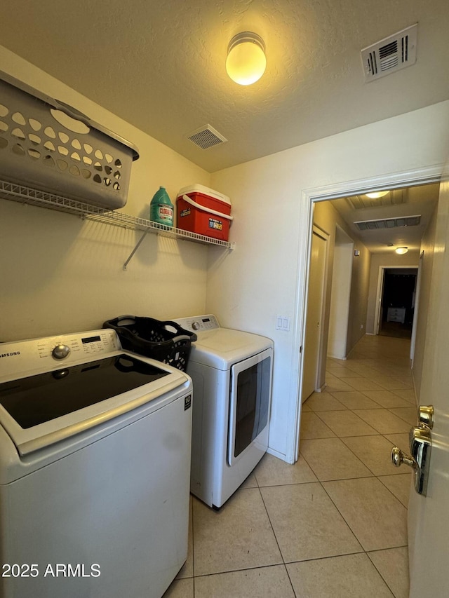 washroom featuring light tile patterned floors, laundry area, washer and clothes dryer, and visible vents