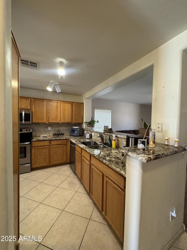 kitchen featuring brown cabinets, visible vents, appliances with stainless steel finishes, light tile patterned flooring, and a sink