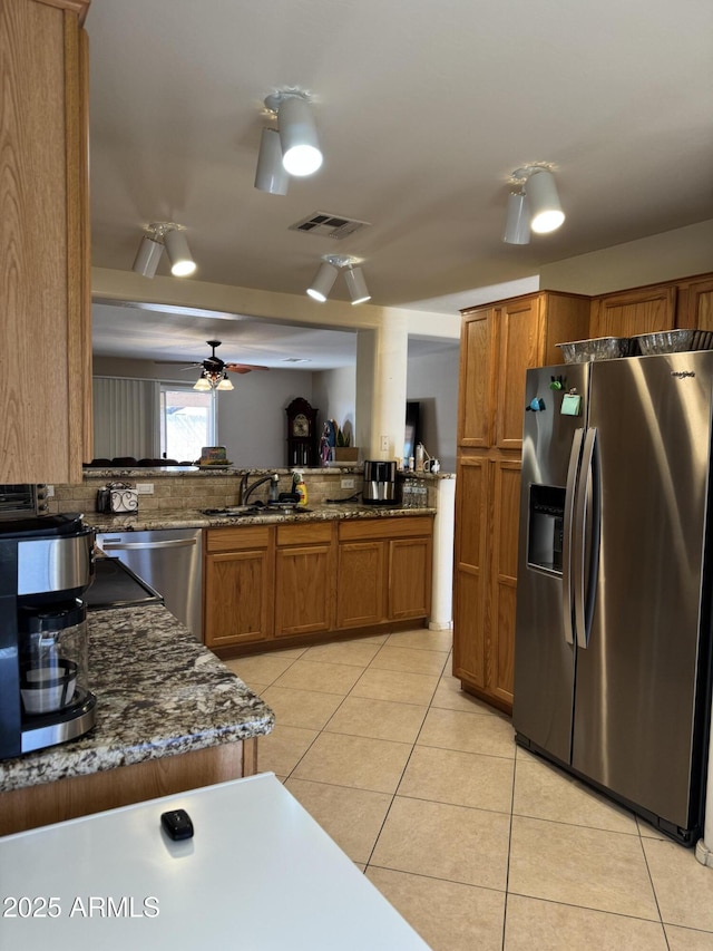 kitchen featuring brown cabinetry, light tile patterned floors, stainless steel appliances, and a sink