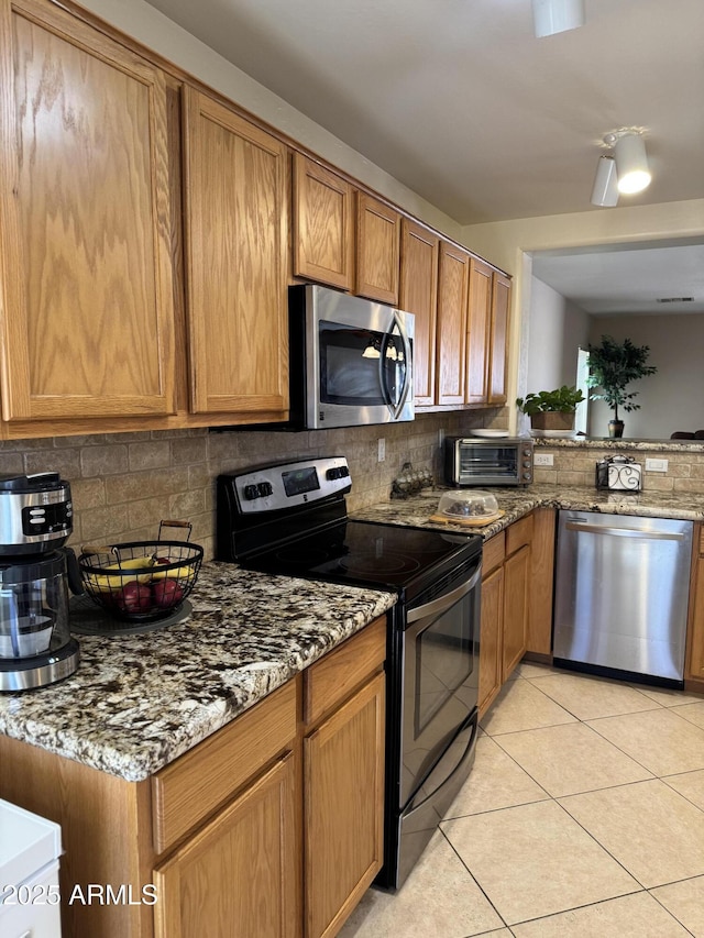 kitchen featuring light stone counters, light tile patterned flooring, a toaster, appliances with stainless steel finishes, and backsplash