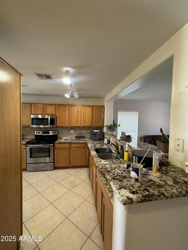 kitchen with stainless steel appliances, tasteful backsplash, visible vents, brown cabinetry, and a sink