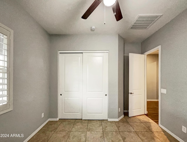 unfurnished bedroom with ceiling fan, a closet, light tile patterned floors, and a textured ceiling