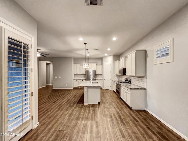 kitchen with tasteful backsplash, dark hardwood / wood-style flooring, pendant lighting, a kitchen island with sink, and appliances with stainless steel finishes