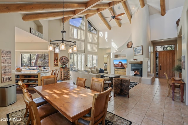 tiled dining space featuring beamed ceiling, ceiling fan with notable chandelier, high vaulted ceiling, and a fireplace