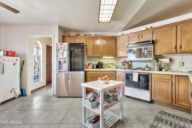 kitchen with tile countertops, stainless steel appliances, lofted ceiling, and light tile patterned flooring