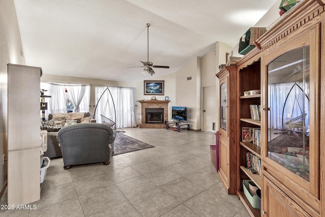 living area featuring light tile patterned floors, a fireplace with raised hearth, ceiling fan, and vaulted ceiling