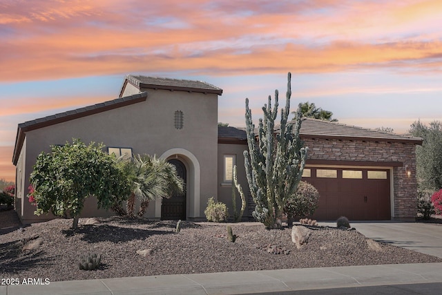 view of front of house featuring stone siding, an attached garage, driveway, and stucco siding