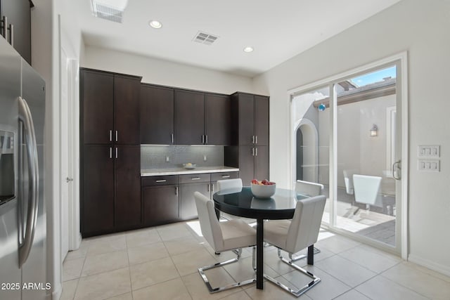 kitchen with light countertops, visible vents, backsplash, dark brown cabinetry, and stainless steel fridge