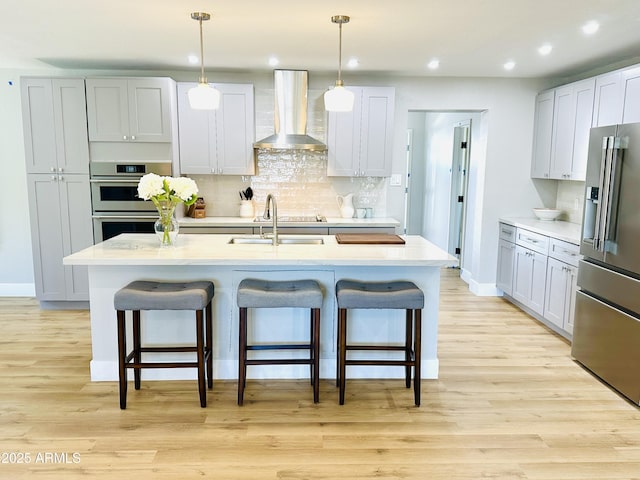 kitchen featuring a sink, appliances with stainless steel finishes, a breakfast bar area, and wall chimney range hood