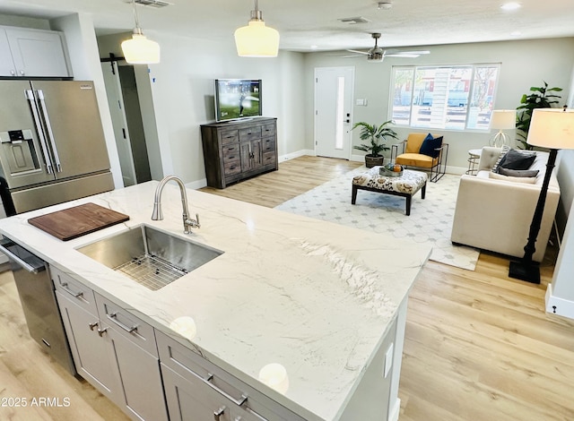 kitchen featuring an island with sink, a sink, decorative light fixtures, stainless steel appliances, and a barn door