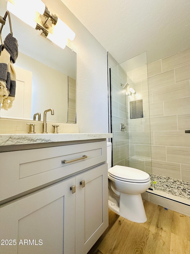 full bathroom with vanity, toilet, wood finished floors, and a tile shower