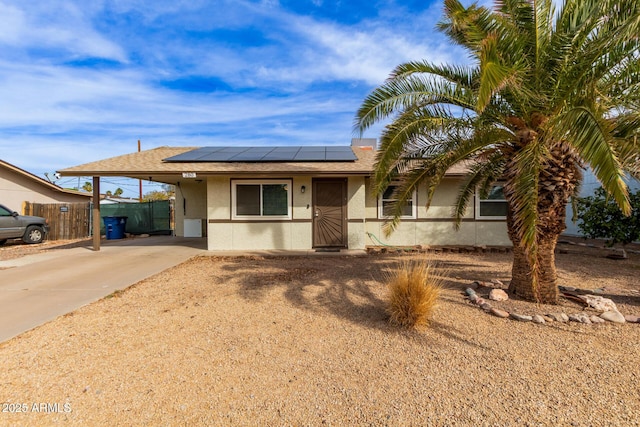 single story home with stucco siding, concrete driveway, roof mounted solar panels, fence, and an attached carport