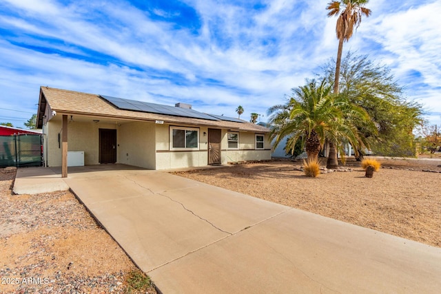 ranch-style home with an attached carport, concrete driveway, roof mounted solar panels, and stucco siding