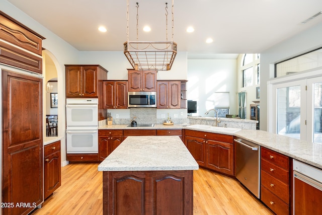 kitchen featuring sink, backsplash, stainless steel appliances, light hardwood / wood-style floors, and a kitchen island