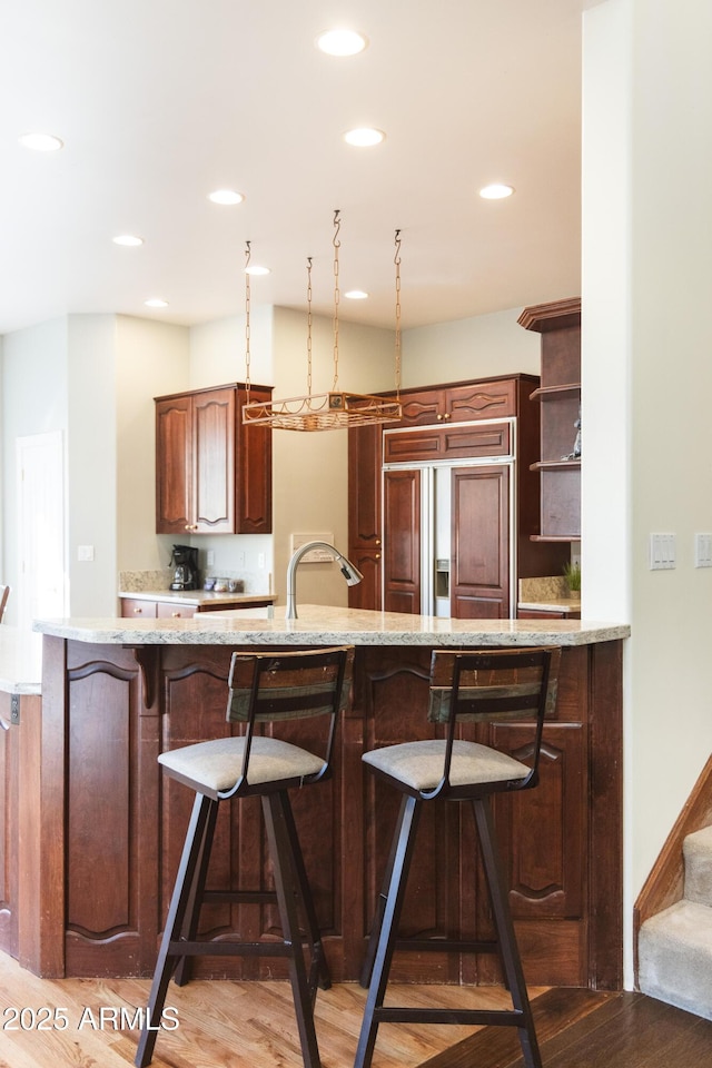 kitchen with sink, wood-type flooring, paneled fridge, and kitchen peninsula