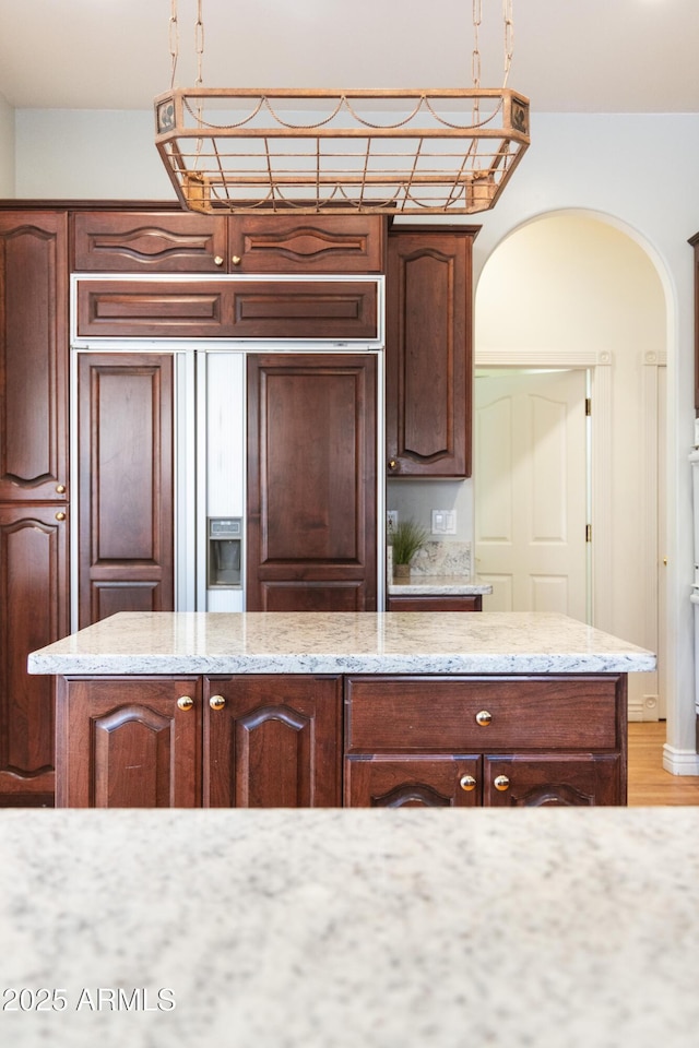 kitchen featuring pendant lighting, a center island, paneled fridge, and light stone counters