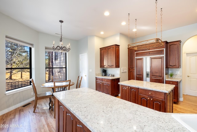 kitchen with pendant lighting, an inviting chandelier, light stone countertops, a kitchen island, and light wood-type flooring