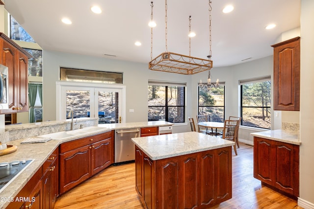 kitchen with sink, a kitchen island, decorative light fixtures, stainless steel dishwasher, and light wood-type flooring