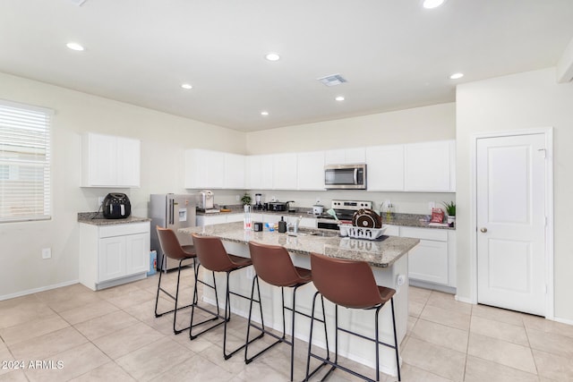 kitchen with light stone countertops, appliances with stainless steel finishes, a center island with sink, white cabinetry, and a breakfast bar area