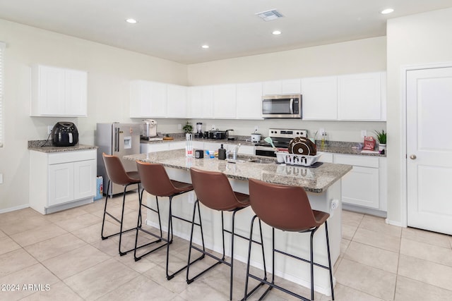 kitchen featuring a kitchen island with sink, white cabinets, light stone countertops, appliances with stainless steel finishes, and light tile patterned flooring