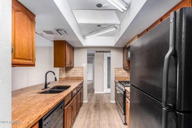 kitchen featuring black appliances, light wood-type flooring, sink, and tasteful backsplash