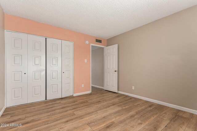 unfurnished bedroom with light wood-type flooring, a textured ceiling, and a closet