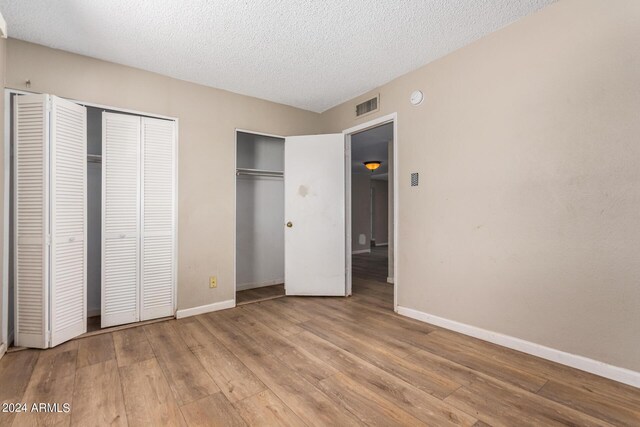 unfurnished bedroom with a textured ceiling, light hardwood / wood-style floors, and two closets