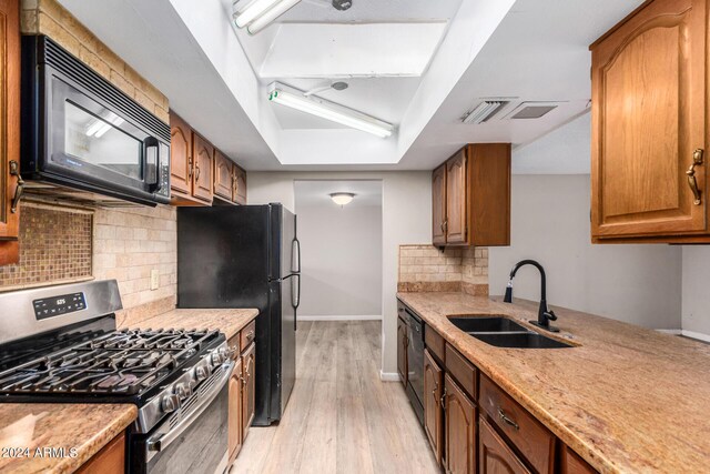 kitchen with sink, a tray ceiling, decorative backsplash, black appliances, and light wood-type flooring