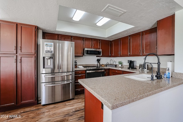 kitchen featuring kitchen peninsula, light wood-type flooring, stainless steel appliances, and a tray ceiling